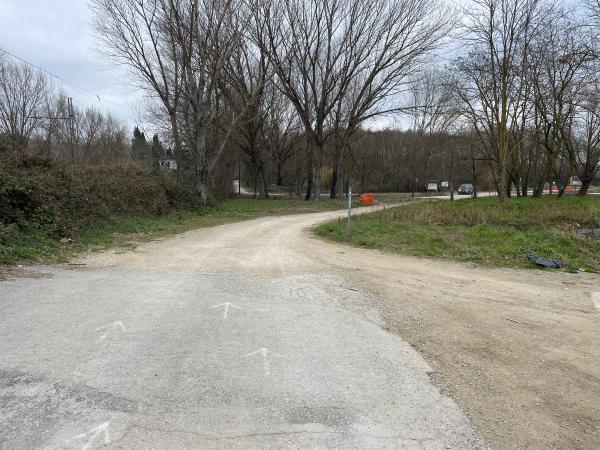 Carrefour entre une piste cyclable et un chemin de terre dans une zone rurale avec des arbres. Sur le sol, des flèches indiquent la direction.